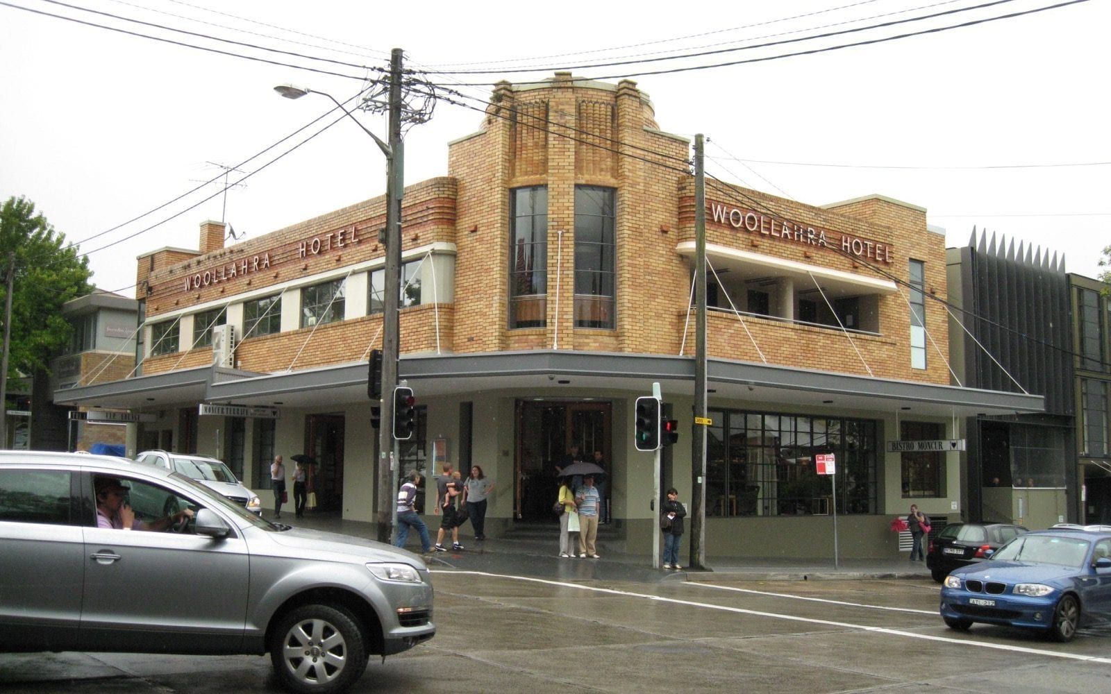 The art deco corner pub in Woollahra, its name in steel lettering above the awning and people crossing beneath it.